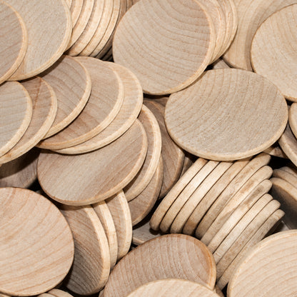 A pile of unfinished light wood round discs, likely plywood or MDF craft blanks, showing natural grain and a pale tan color.