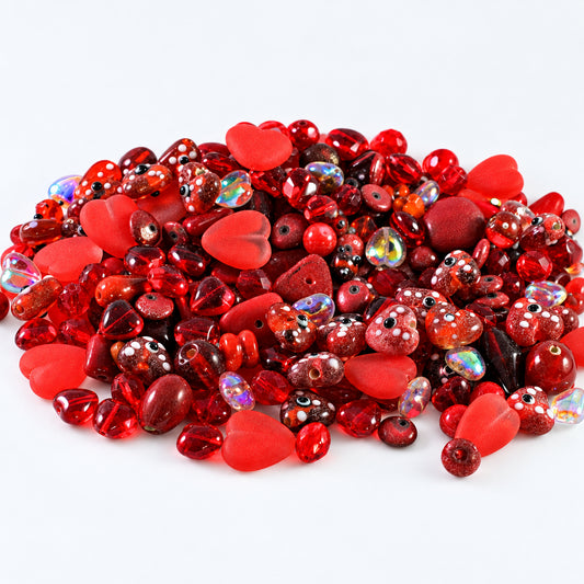 A pile of red heart-shaped and round glass beads with various finishes, including glossy, matte, and iridescent, on a white background.