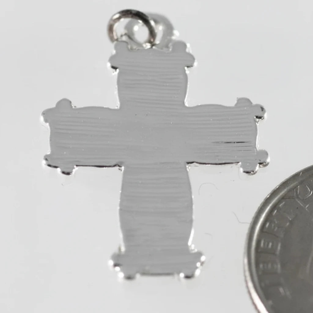 A silver cross pendant with a textured finish and a small hanging loop at the top, shown on a light gray background with a coin partially visible at the bottom right for scale.