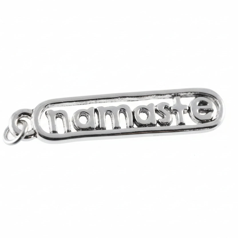 A silver metal charm spelling 'namaste' in raised letters, shown close-up against a white background with a coin partially visible on the left for scale.