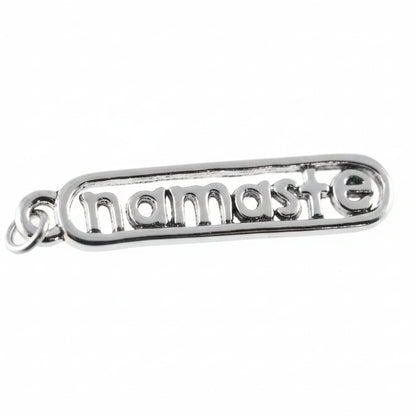A silver metal charm spelling 'namaste' in raised letters, shown close-up against a white background with a coin partially visible on the left for scale.