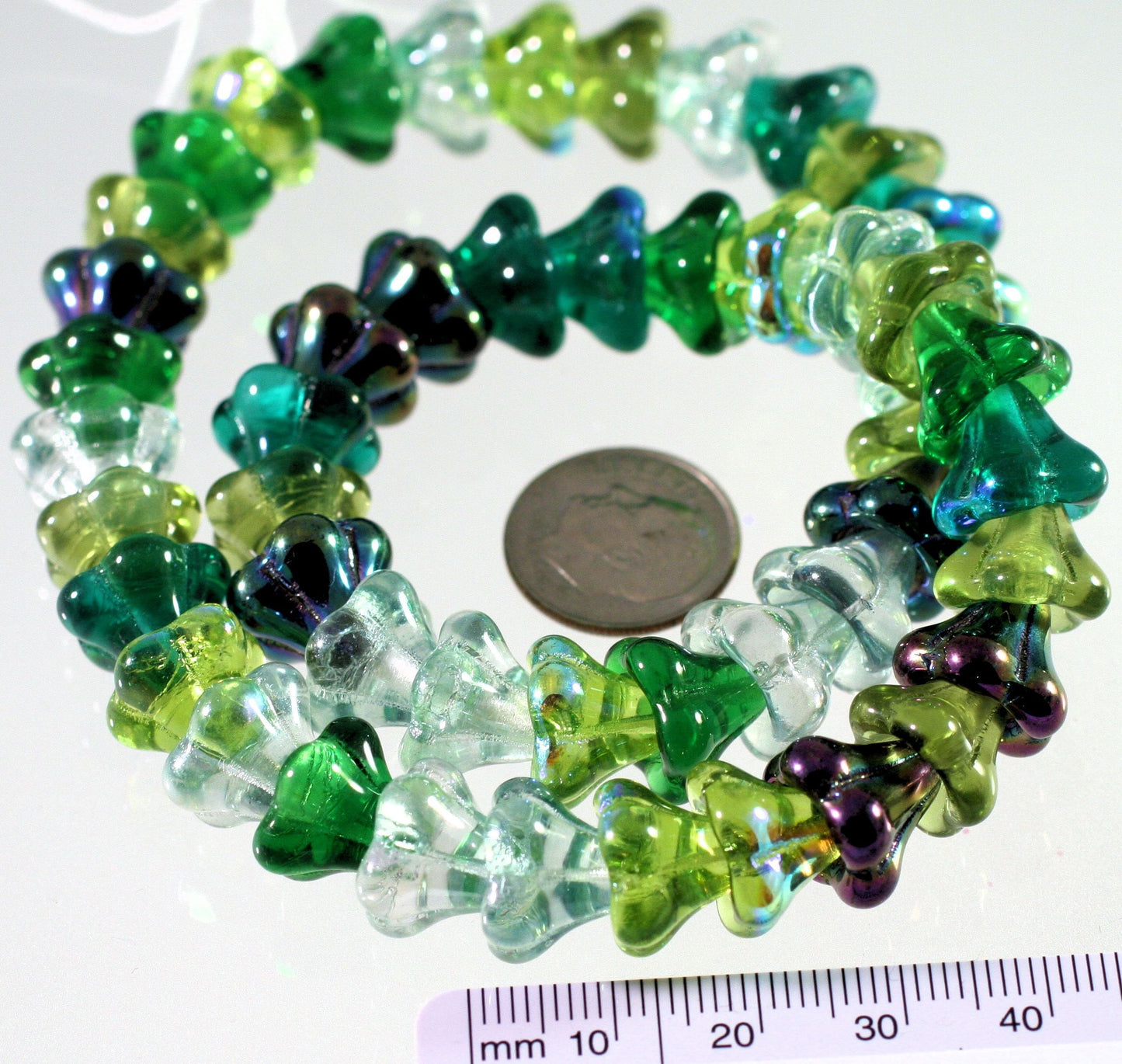 Colorful beads with a coin and ruler for size reference on a white background