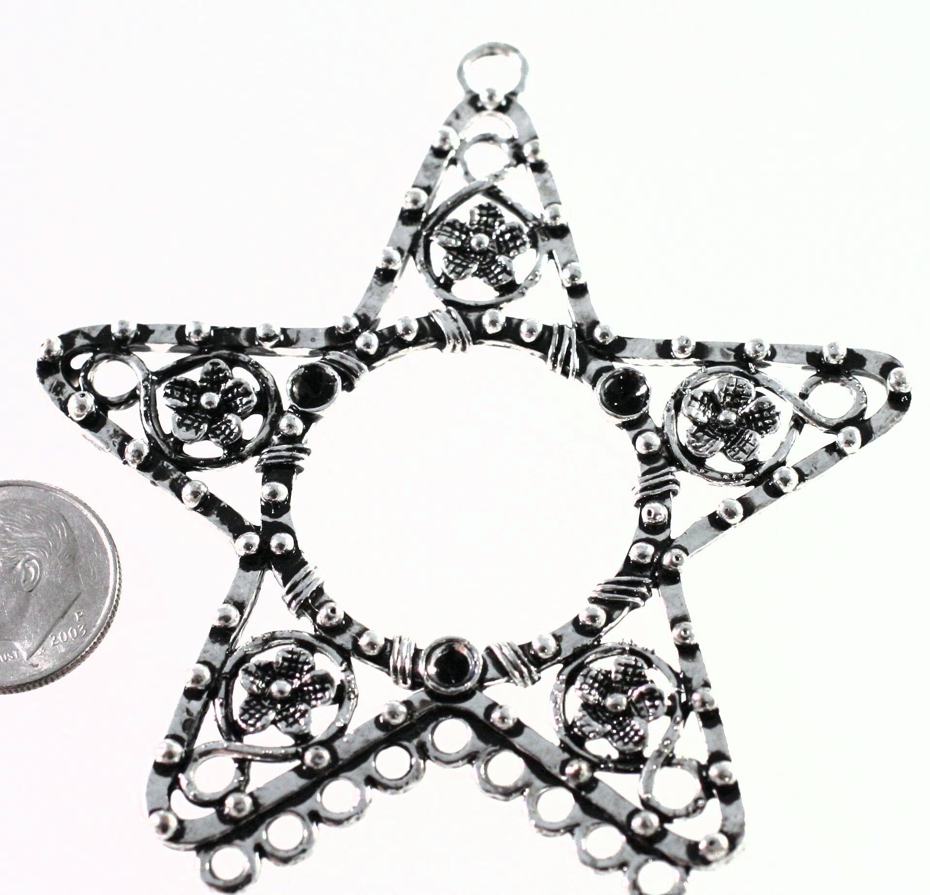 Star-shaped silver pendant with intricate designs on a white background, next to a coin for scale.