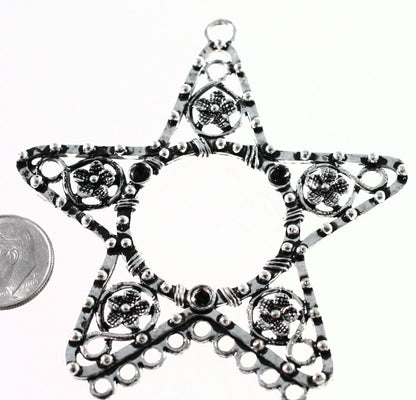 Star-shaped silver pendant with intricate designs on a white background, next to a coin for scale.