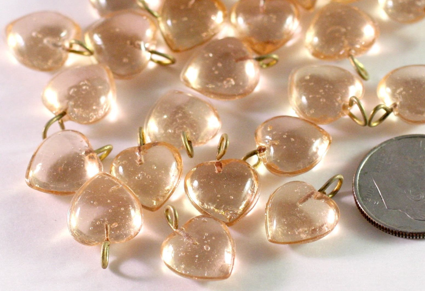 Heart-shaped beads on a white background, next to a dimefor scale.