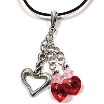 A silver-toned heart charm necklace featuring a large open heart pendant, a smaller heart charm, and two faceted red hearts with pink crystal accents on a black cord.