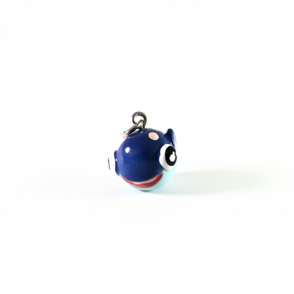 A close-up of a glossy blue character charm with a silver metal clasp, featuring large white and black eyes, a small beige dot, and a red band at the bottom, set against a plain white background.