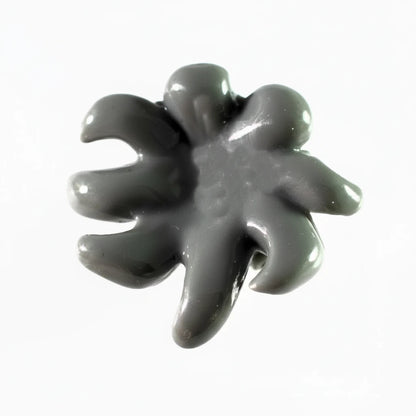 A glossy dark gray stone or resin cabochon with a five-petal, flower-like or starburst shape, shown on a plain white background.