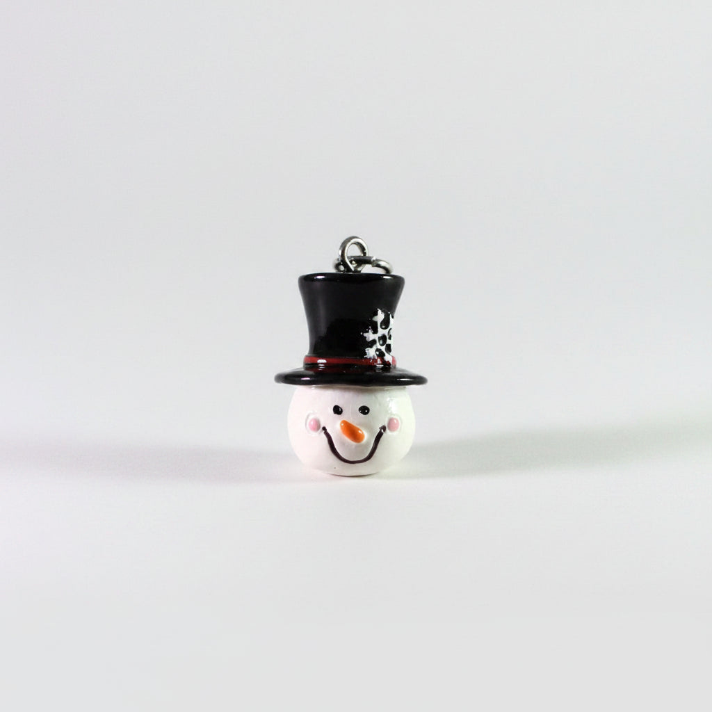 A small snowman ornament or charm with a glossy white face, black top hat, red band, and silver hanging loop on a plain light background.