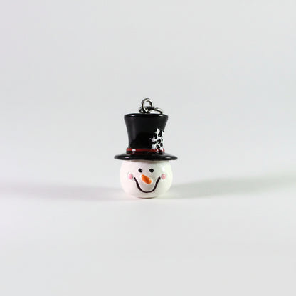 A small snowman ornament or charm with a glossy white face, black top hat, red band, and silver hanging loop on a plain light background.