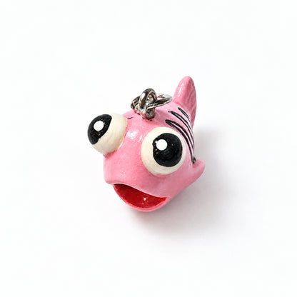 A pink fish-shaped keychain charm with large black and white cartoon eyes, a red mouth, and a silver metal ring at the top, shown on a plain white background.