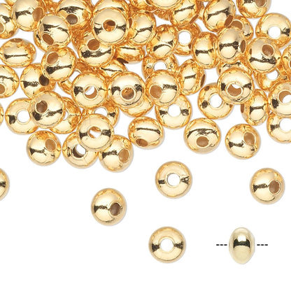 Gold metallic round spacer beads with a central hole, scattered on a white background with a few individual beads and a dashed line indicating size.
