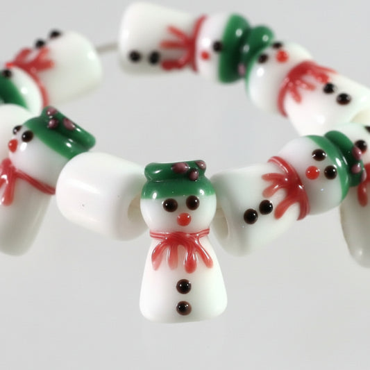 Close-up of a string of festive glass beads shaped like snowmen, featuring white bodies, green hats and scarves, red accents, and black facial details.
