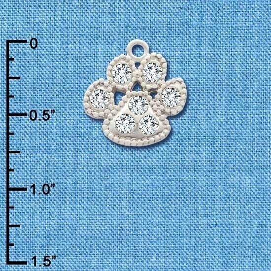 A small paw-shaped jewelry charm with clear rhinestones on a textured blue background, with a black inch ruler on the left side for scale.