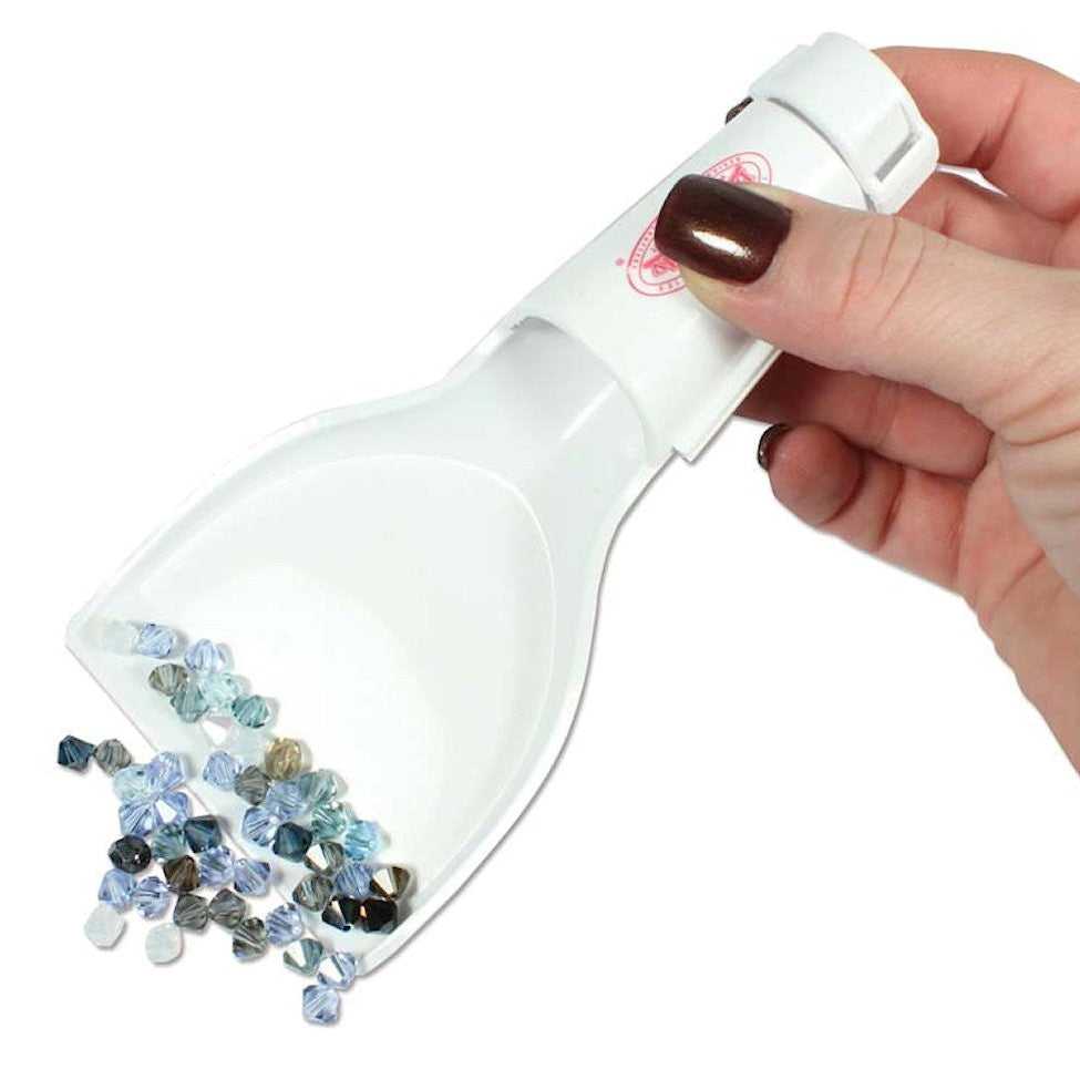 Hand holding a small white scoop filled with gemstones against a white background
