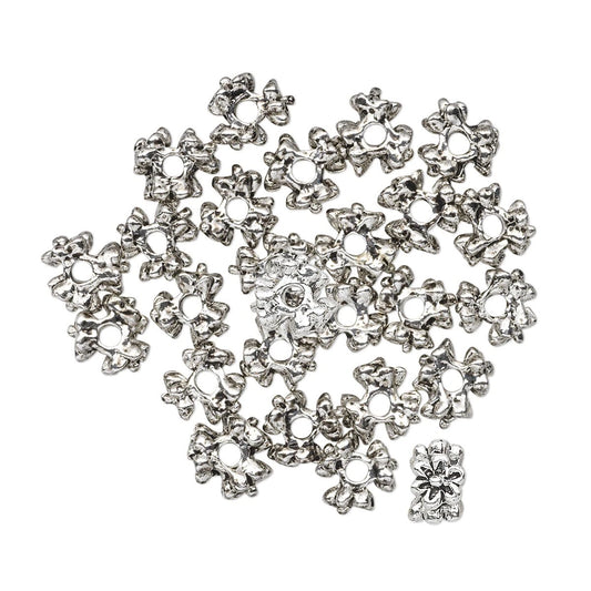 A pile of silver-toned metal flower-shaped beads with circular holes, arranged on a plain white background.