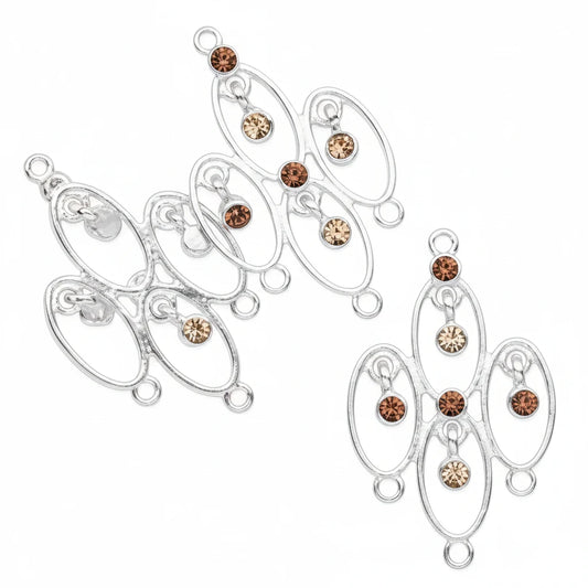 A pair of silver-toned filigree jewelry charms with oval loops and small clear and amber-brown rhinestones, displayed on a solid dark gray background.
