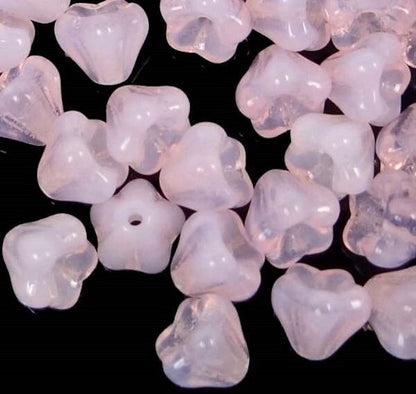 A pile of small translucent pale pink beads with a floral or clover-like shape, shown on a black background.
