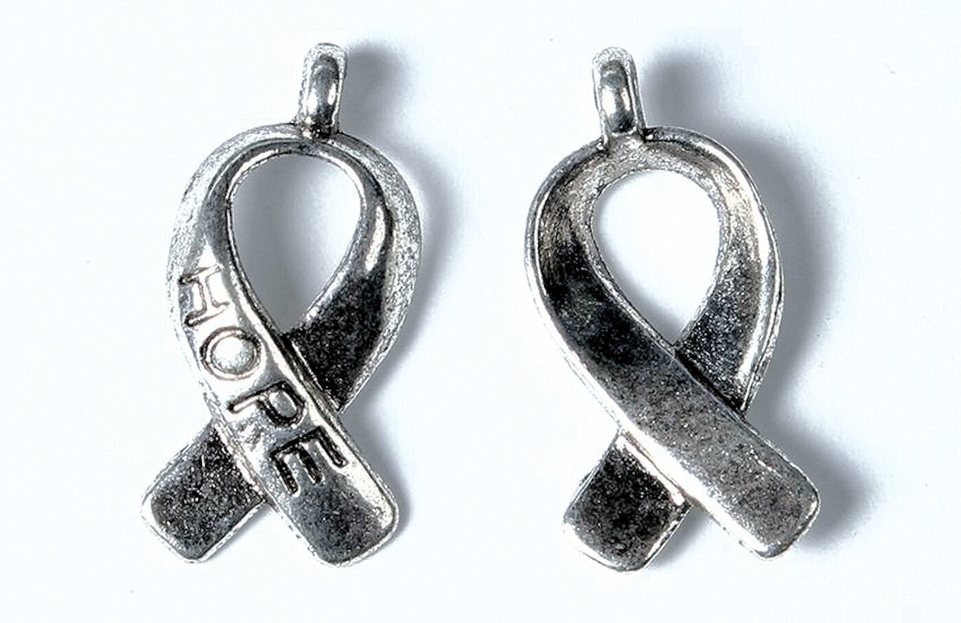 Two silver awareness ribbon pendants on a white background, one engraved with the word 'HOPE'.