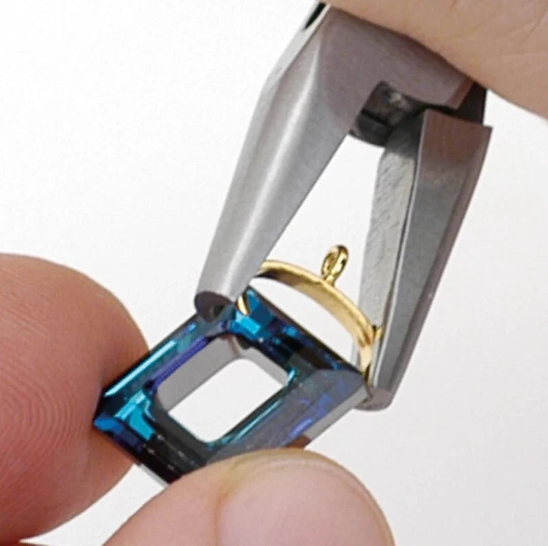 Close-up of a hand using metal ring stretchers to expand a gold ring over a blue faceted crystal setting.