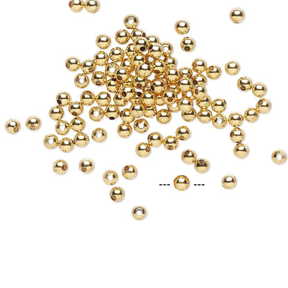 A pile of small shiny gold metallic beads scattered on a plain white background, with a few loose beads visible around the edges and a dashed line near the bottom center.