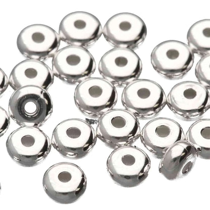 A pile of shiny silver metallic round beads with a central hole, photographed on a plain white background.