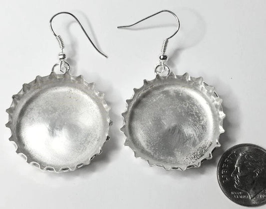 A pair of handmade silver bottle cap earrings with fishhook wires, displayed on a white background next to a US quarter coin for scale.
