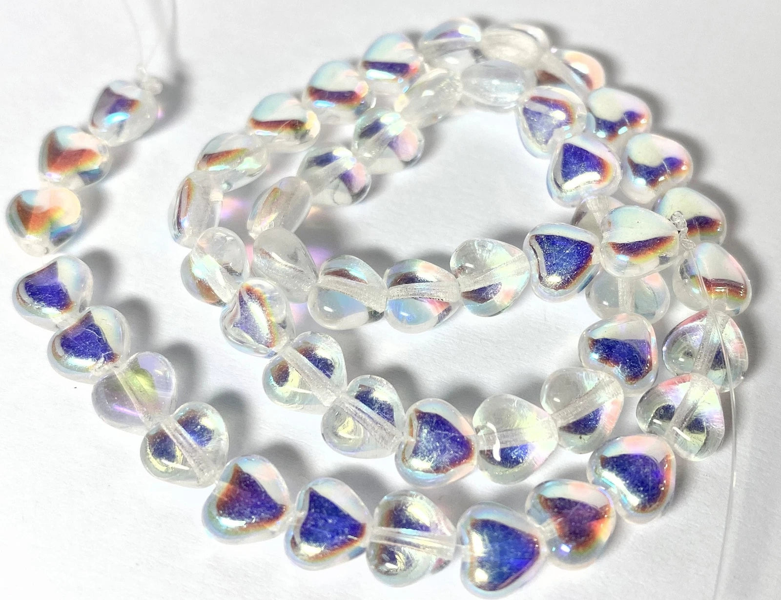Heart-shaped glass beads with an iridescent white and blue finish, arranged in a loose coil on a white background.