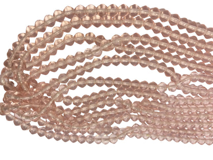 Multiple strands of faceted rose quartz beads in a light pinkish-tan hue, arranged in curved loops on a plain light background.