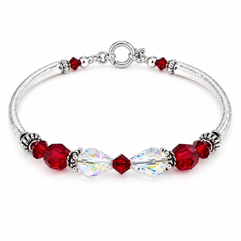A silver-toned beaded bracelet featuring faceted deep red beads, a large clear teardrop crystal, and small silver spacer beads, displayed on a light beige surface.