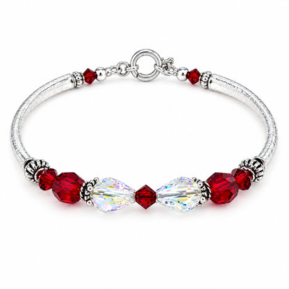 A silver-toned beaded bracelet featuring faceted deep red beads, a large clear teardrop crystal, and small silver spacer beads, displayed on a light beige surface.
