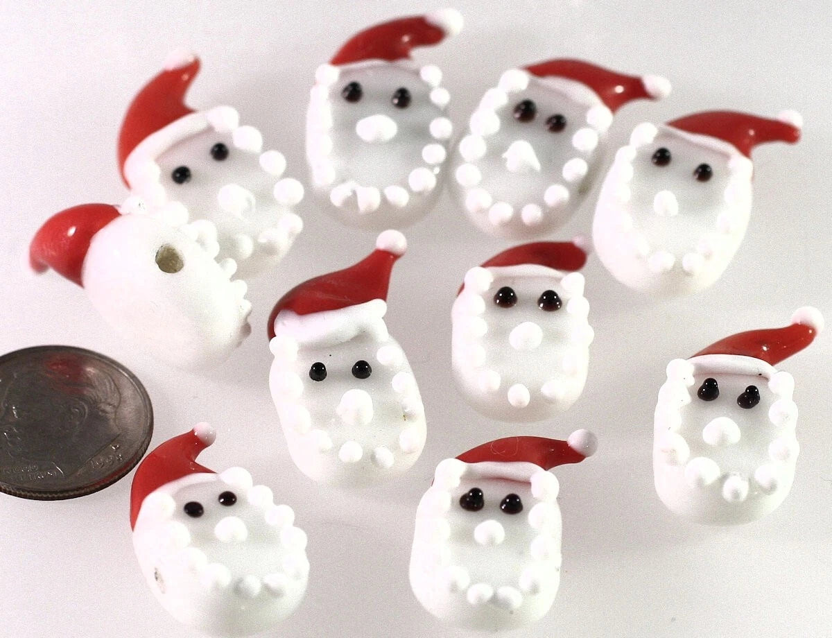 Multiple small white Santa Claus face charms with red hats and black eyes, arranged on a white background with a coin for scale.