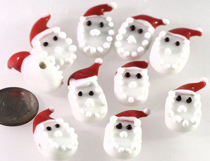 Multiple small white Santa Claus face charms with red hats and black eyes, arranged on a white background with a coin for scale.
