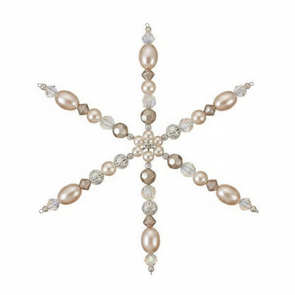 A handmade beaded snowflake ornament held in a person's hand. The ornament features iridescent white pearls, faceted clear beads, and small metallic gold and silver beads, set against a plain light background.