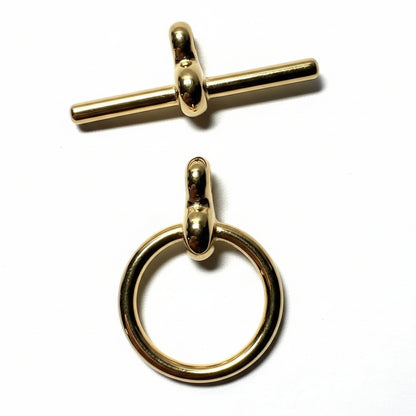 Two small gold-tone jewelry findings on a white surface: a toggle clasp at the top and a ring pull at the bottom, with a U.S.